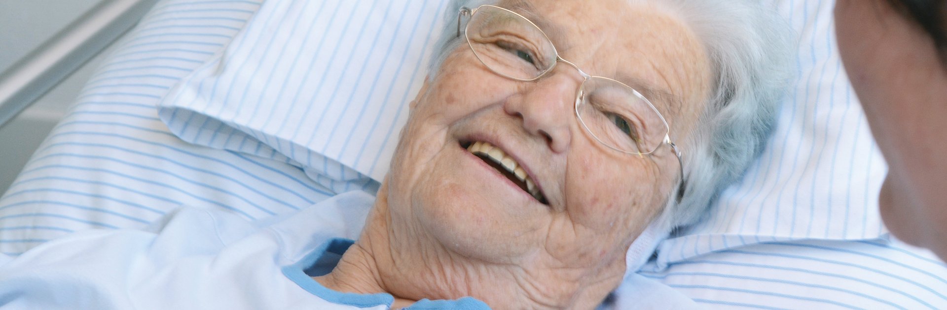 Seniorin im Bett spricht mit einer Pflegerin